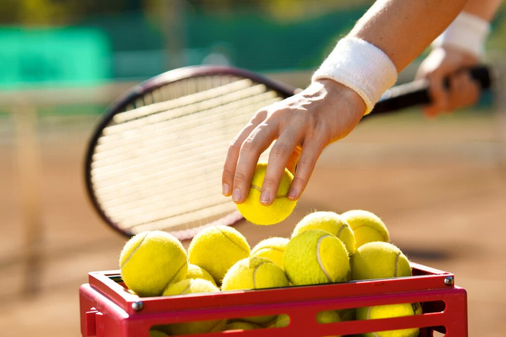 An image of a Tennis player at the court taking a ball from a basket