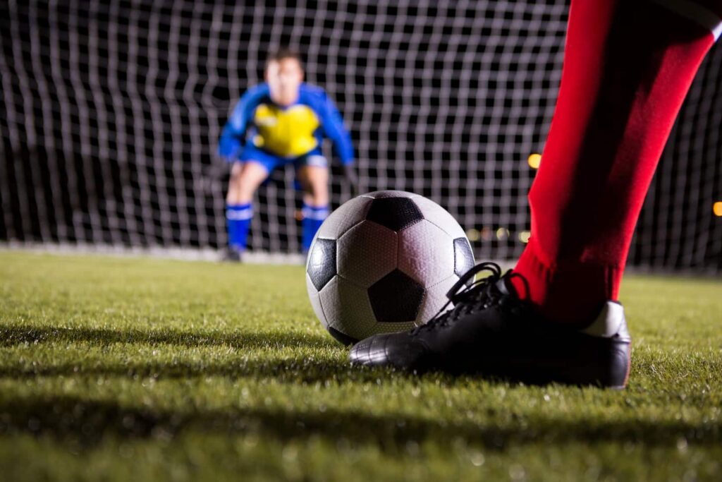 An image of a Low section of soccer player with ball against goalkeeper.
