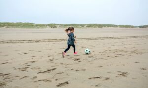 An image of a little girl playing soccer on the beach.