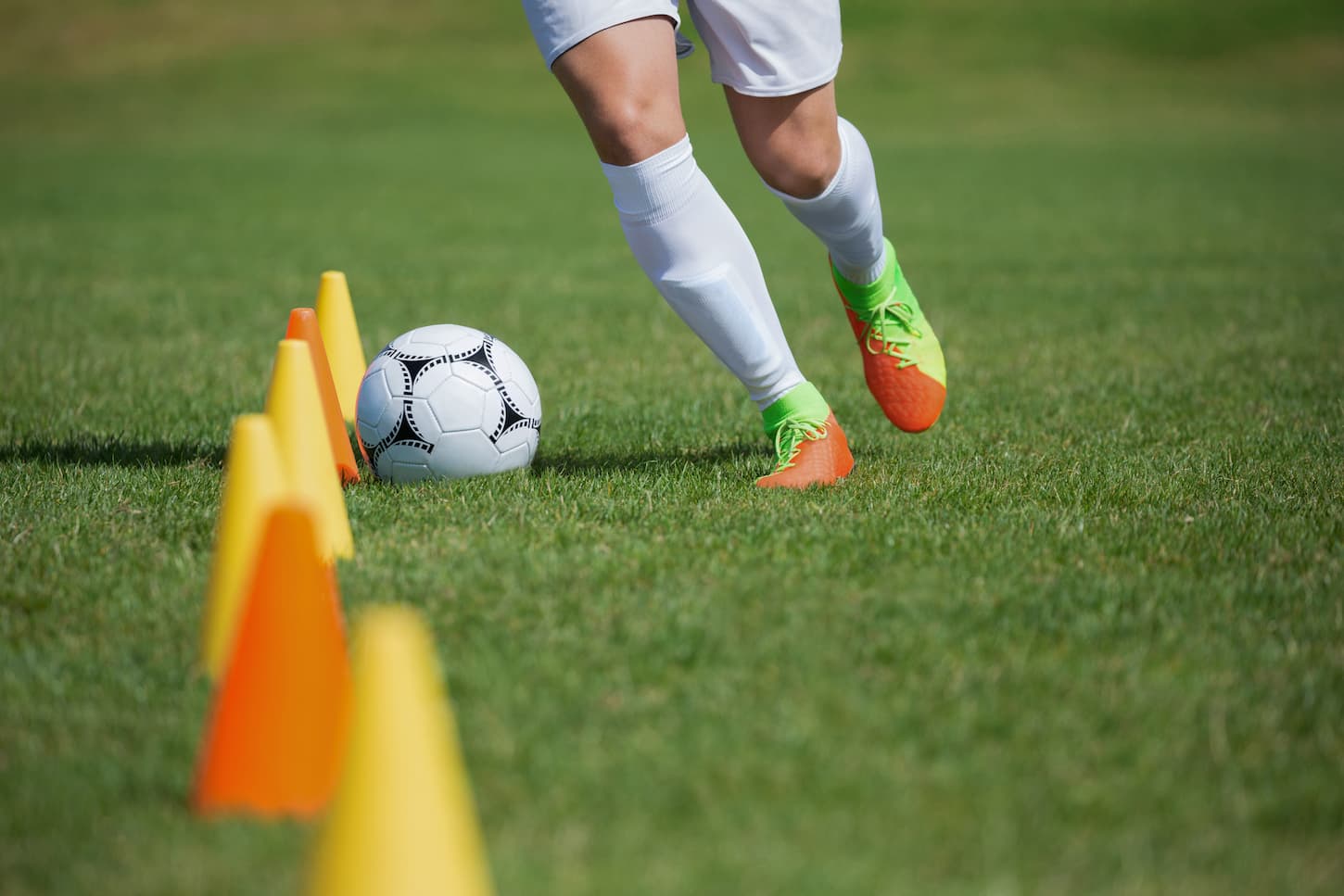 An image of a soccer player dribbling through the cones in a soccer field.