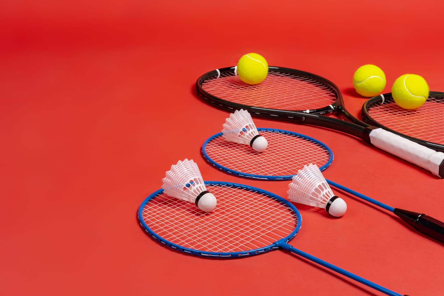 An image of rackets for tennis and for badminton on a red background.