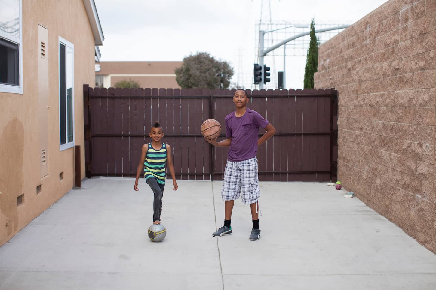 An image of two boys in a yard with a basketball and football.
