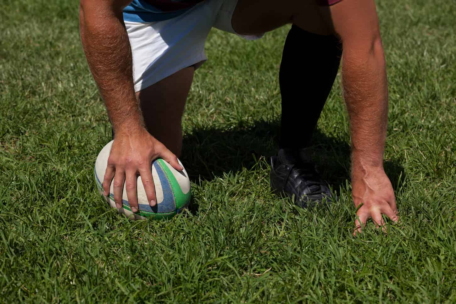 An image of a Player crouching with rugby ball on field.