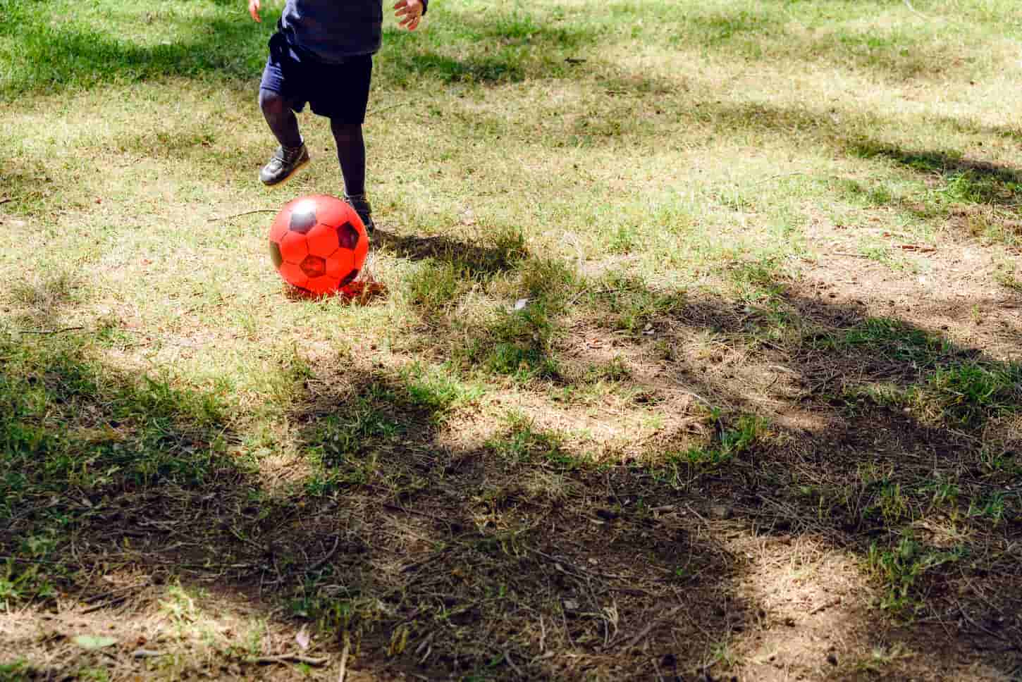 An image of a Child playing with a red plastic football ball.