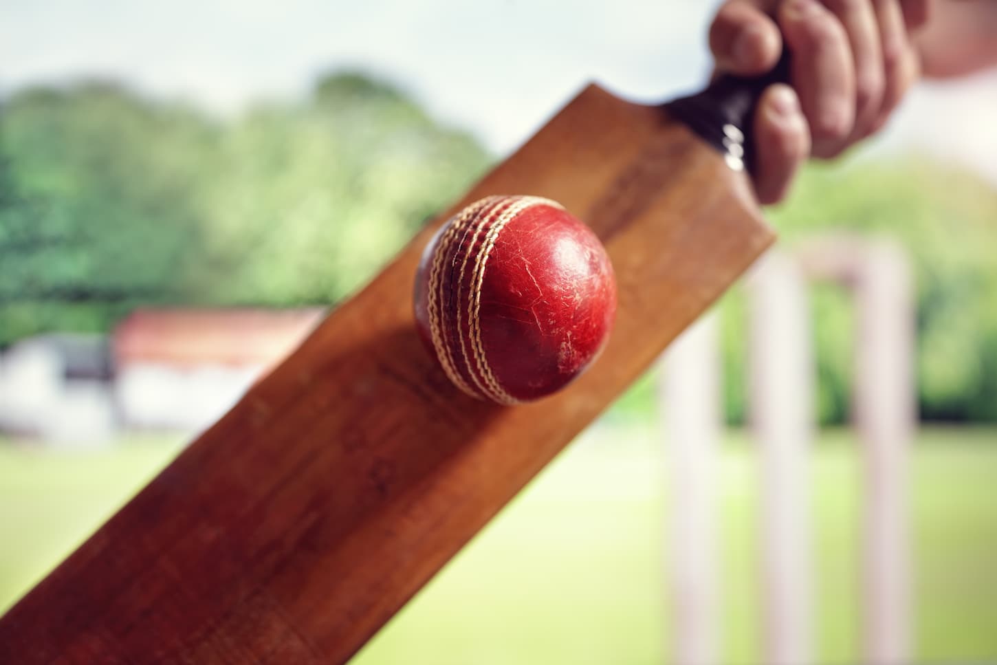 An image of a Cricket batsman hitting a ball shot from below with stumps on the cricket pitch.