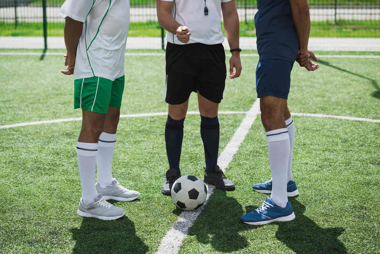 An image of a referee and soccer players on a soccer pitch starting game.