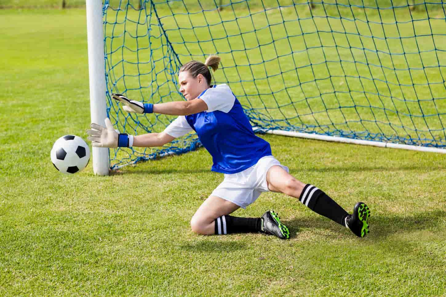 An image of a Female goalkeeper in her complete gear saving a goal during a game.
