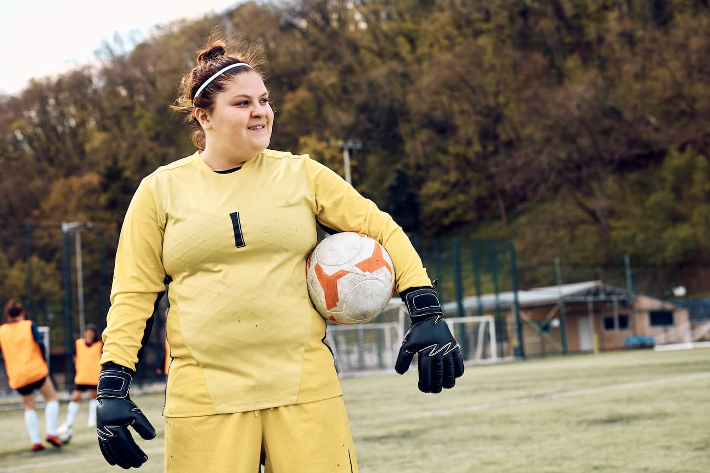 An image of a Female soccer goalie with a ball during sports training at the stadium looking away.