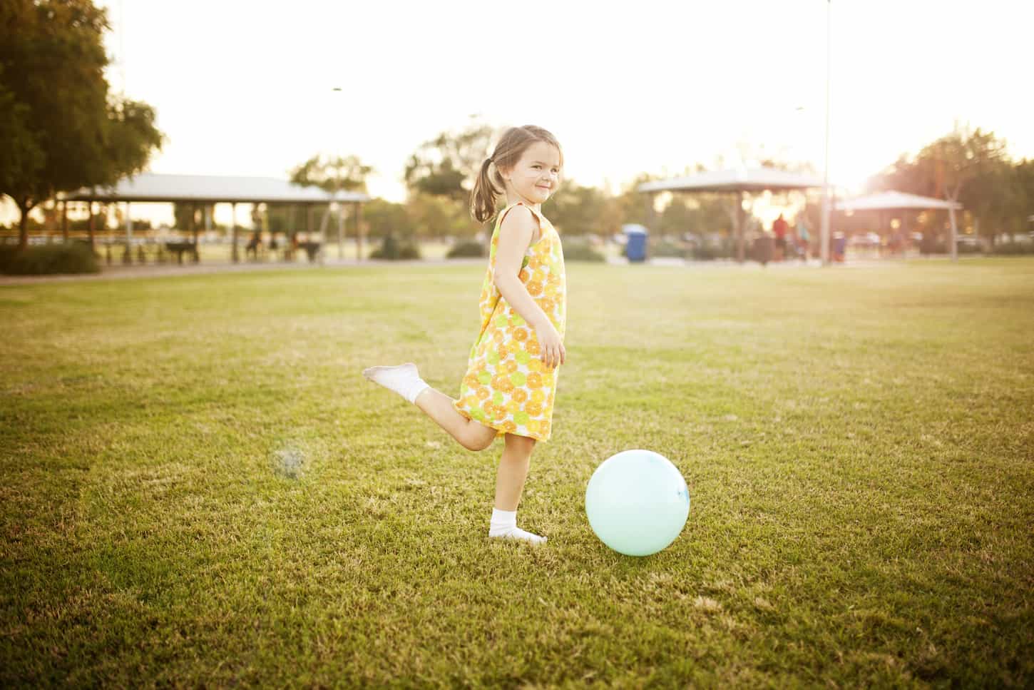 An image of a Girl kicking a ball at the park.