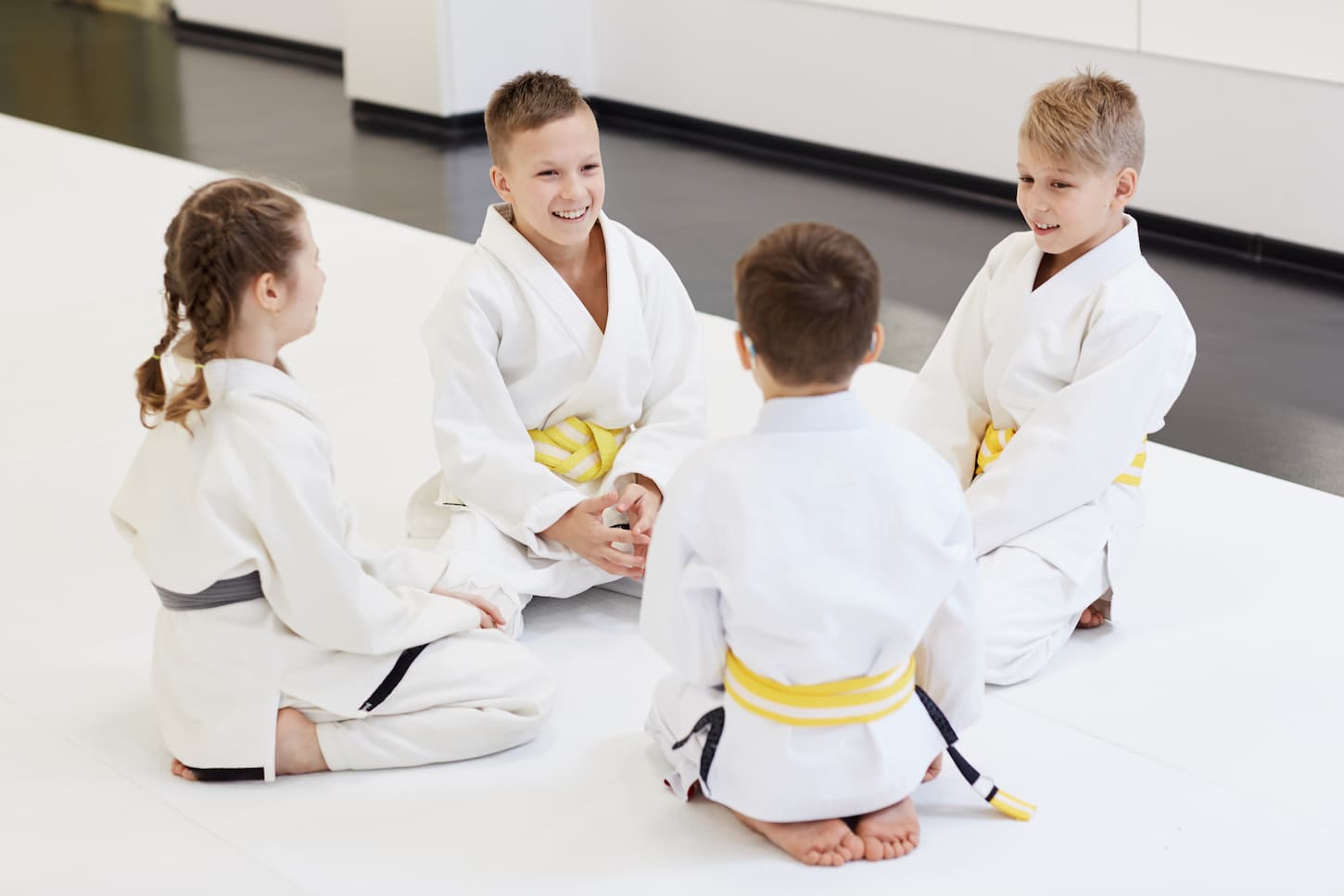 An image of a Group of children sitting on the floor together and talking to each other before sports training in karate in the gym.