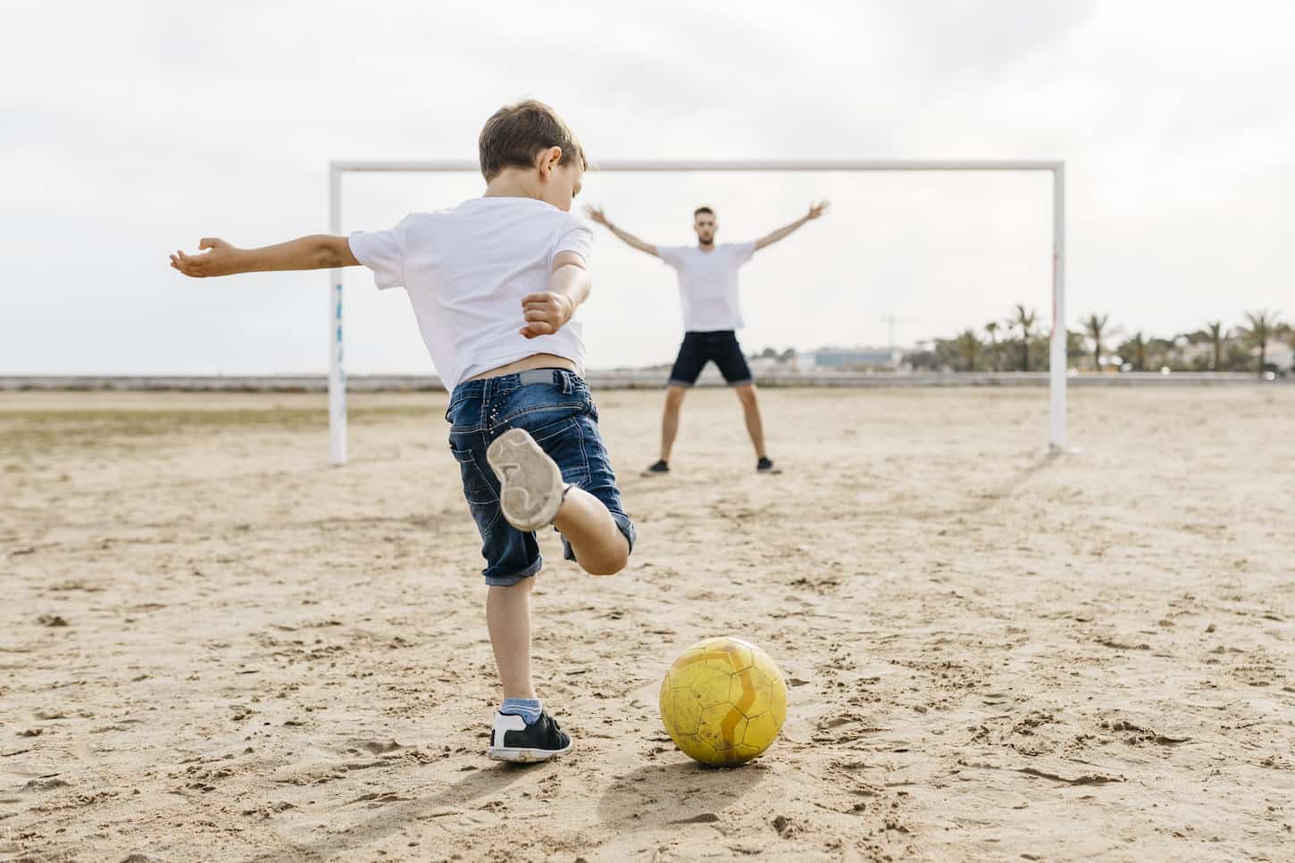 An image of a Man and boy playing soccer on the beach.