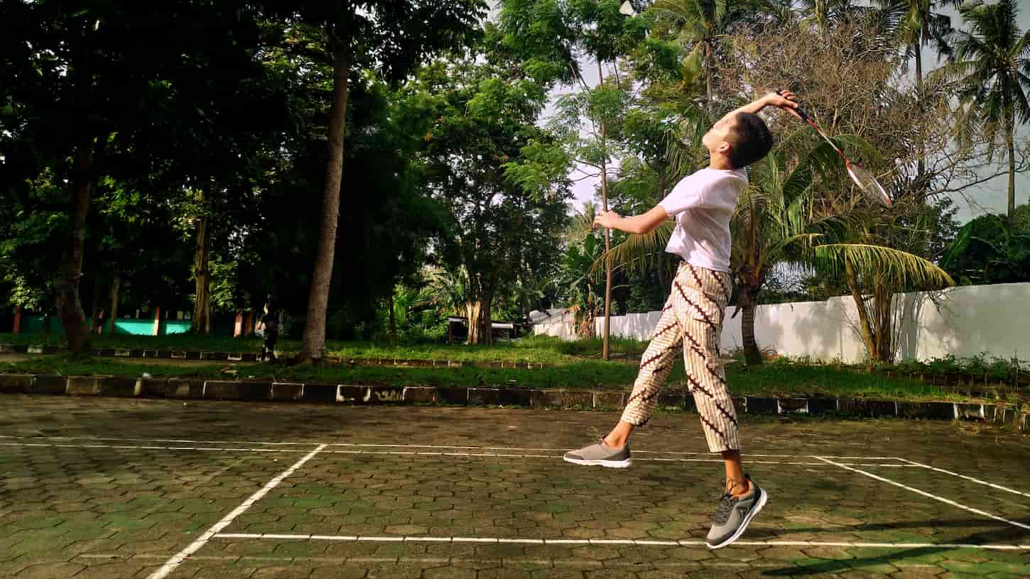 An image of a young man playing badminton on an outdoor badminton court.