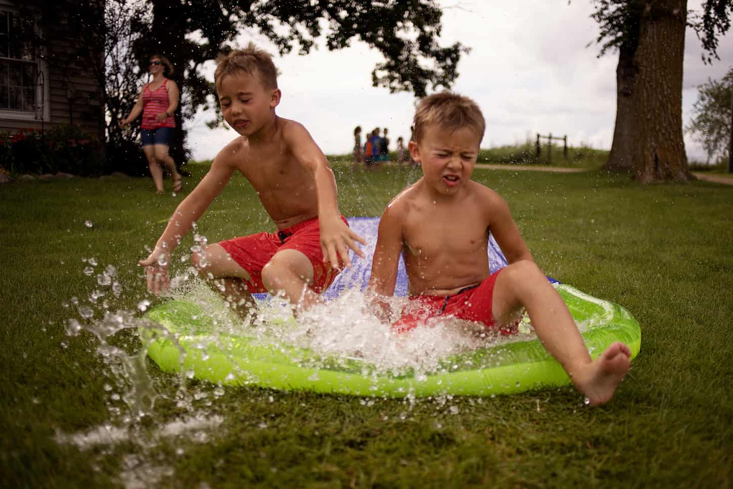 An image of Twin brothers using the slip-and-slide on a summer day.