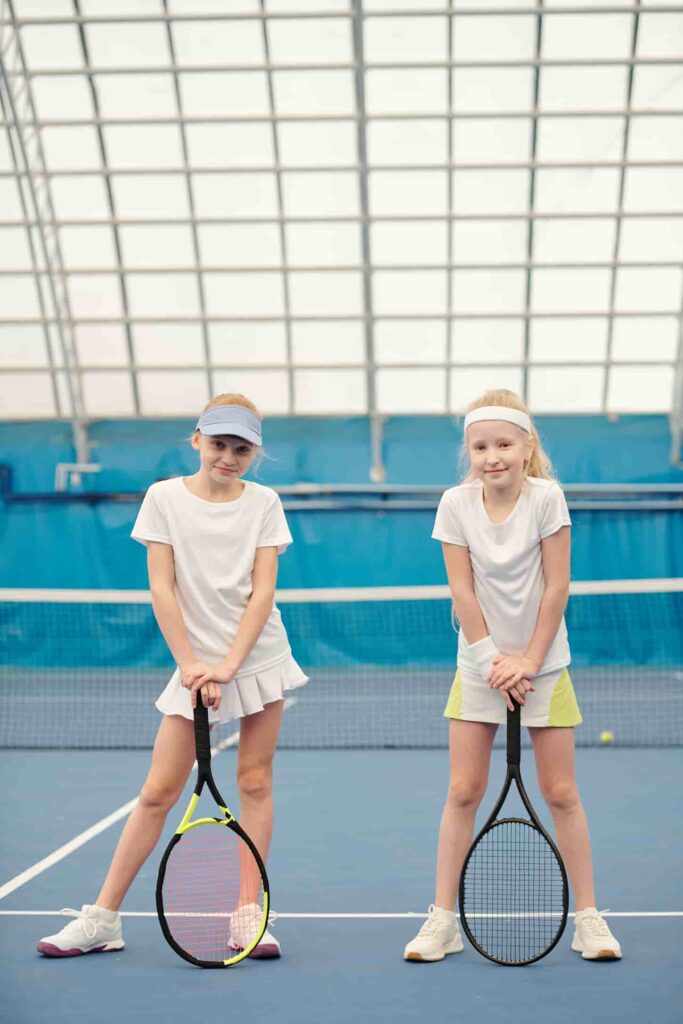 An image of Two active teenage girls in white sportswear standing on a tennis field at the stadium.