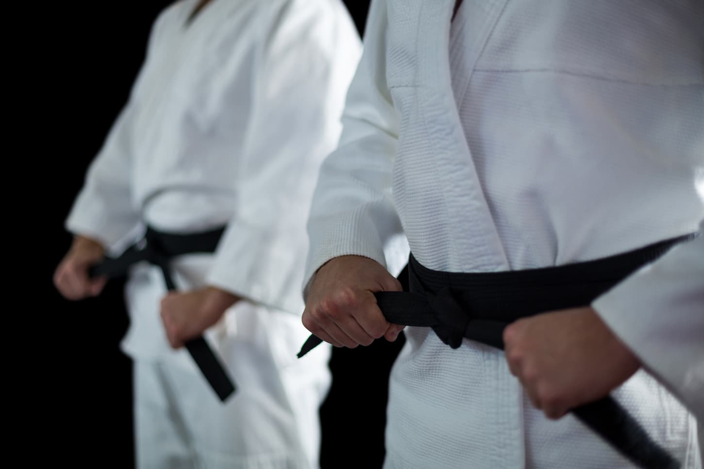 An image of a Midsectiona of Two karate fighters performing karate stances against a black background.