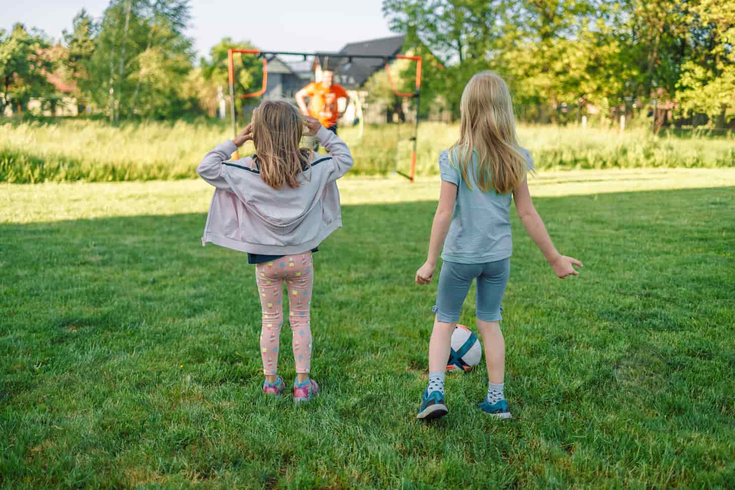 An image of Two girl kids playing with a ball outdoors in a park on blurred background. Fun with friends and a football.
