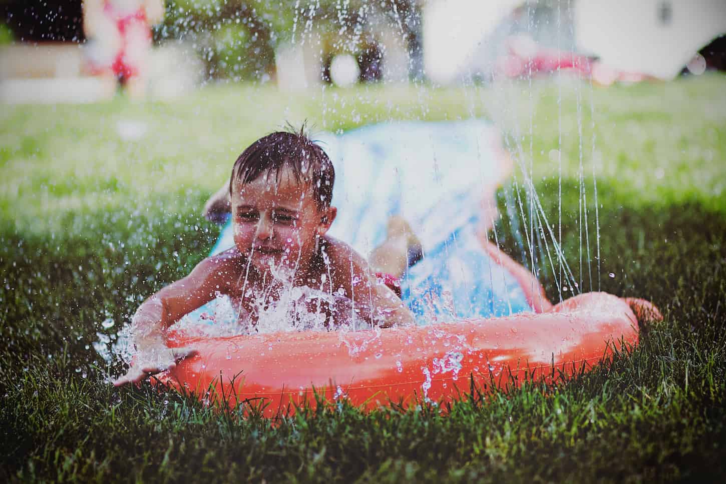 An image of a young boy sliding down and splashing on an outdoor slip-and-slide. Make a great expression and have fun on a warm summer day.