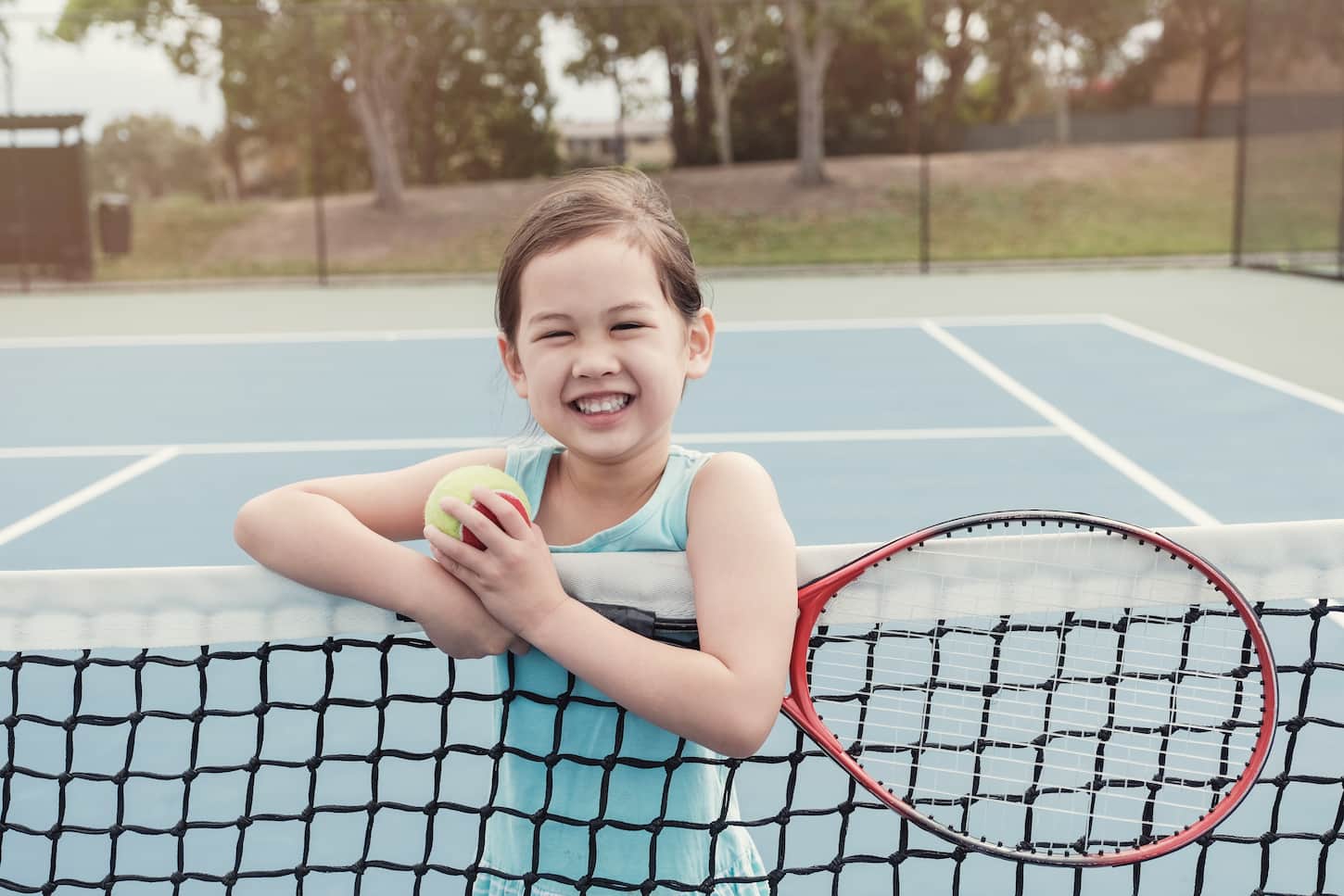 An image of a Young Asian girl tennis player on an outdoor blue court.