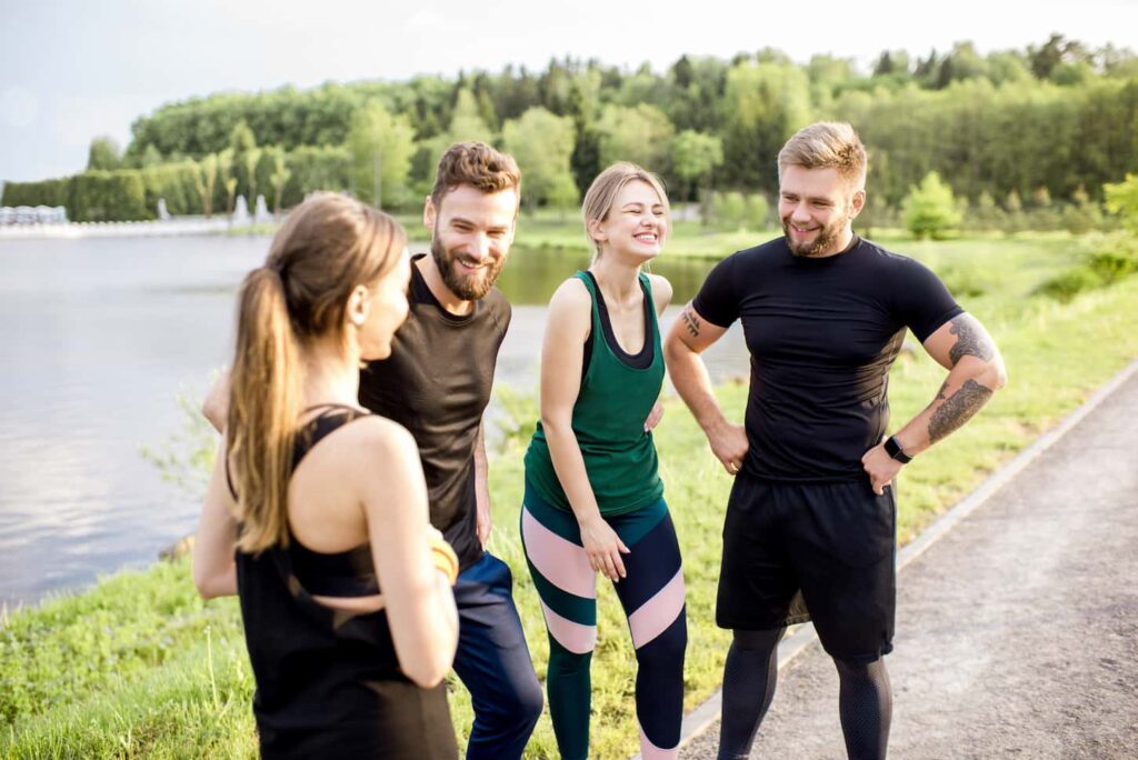 An image of Sports team having fun standing together after the training outdoors in the park near the lake.