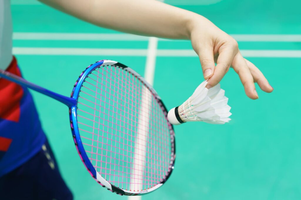 An image of a woman holding a badminton racket ready to hit shuttlecock.