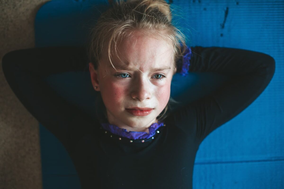 An image of a Preteen athlete in stretching class, a girl lying on the yoga mat and barely crying after a hard workout.