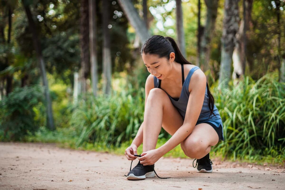 An image of a smiling Asian sports girl tying her shoelaces in the park.