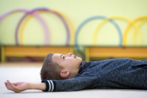 An image of a Young child boy laying down and relaxing while resting on the floor inside sports room in a school.