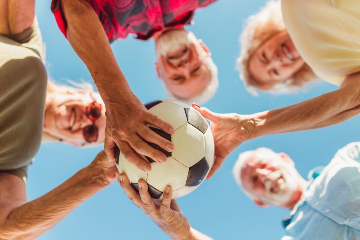 An image of a Low angle view of a group of cheerful active senior people having fun playing football, gathered in a circle, holding a soccer ball all together before the match.