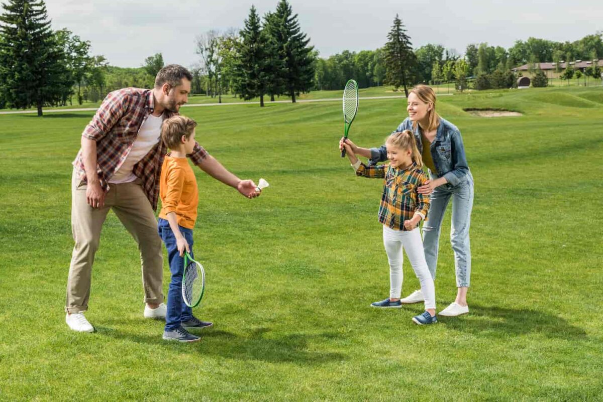 An image of Parents teaching little kids how to play badminton at a park.
