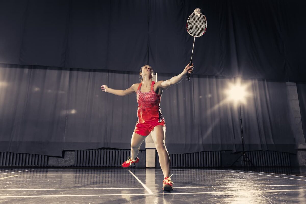 An image of a Young woman playing badminton over a gym background.